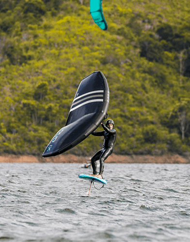 A young man practicing wing foiling; in the background, the sea and vegetation can be seen