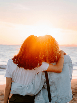 Two young women embracing with the sunrise in the background